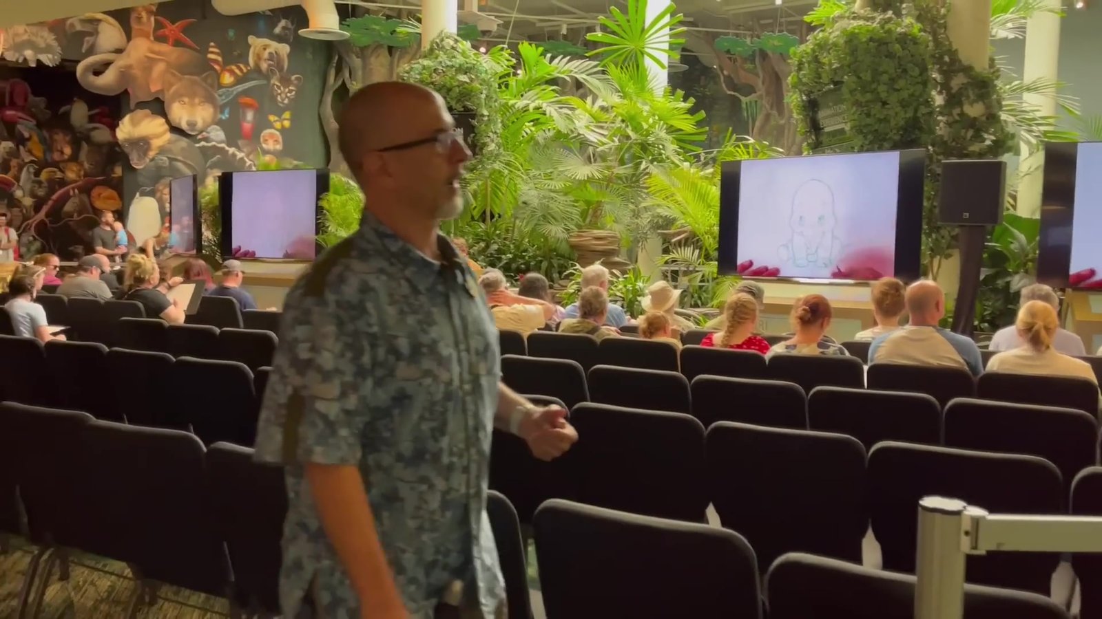 Animador da Disney conduzindo a Animation Experience, com a plateia sentada e as telas com o desenho