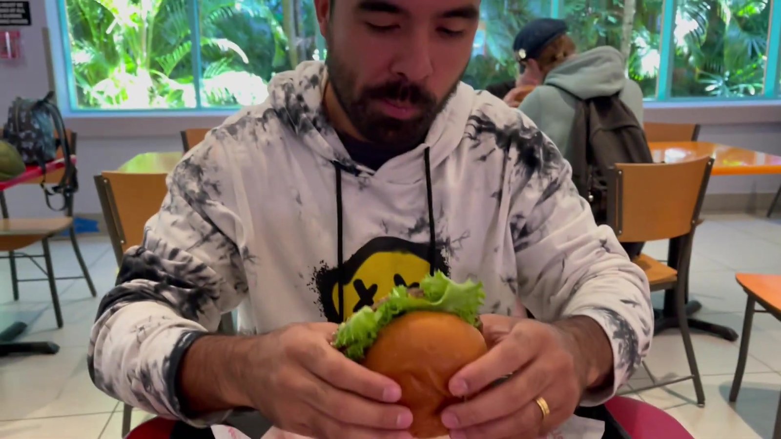 Gustavo segurando o Krusty Burger com alface e pão brioche na mesa do Fast Food Boulevard