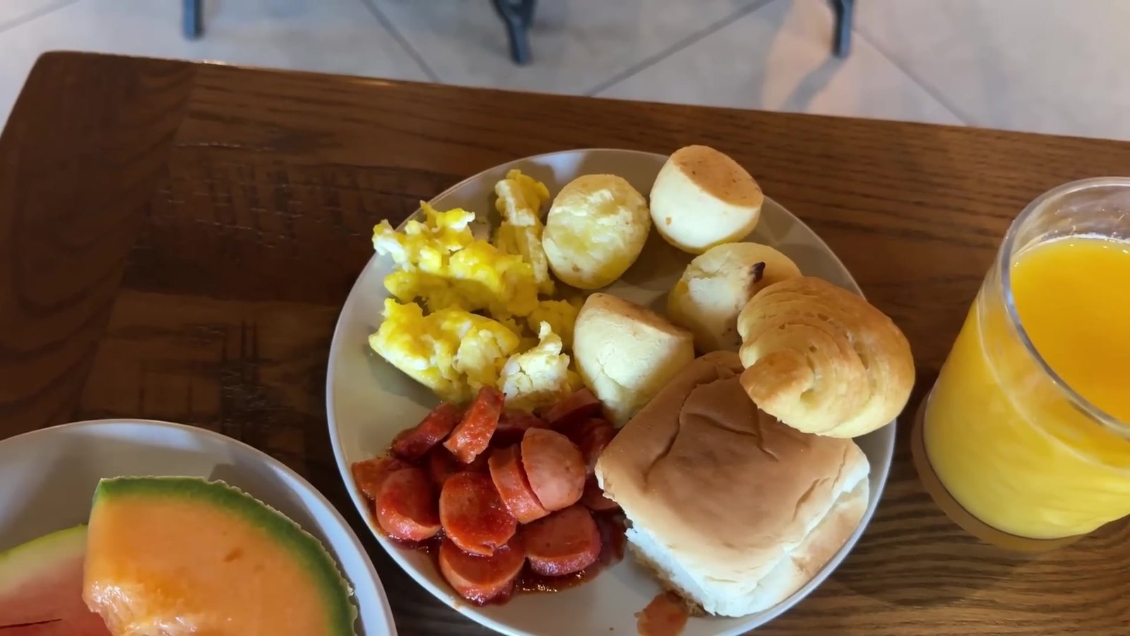 Prato montado com ovos mexidos, pão de queijo, salsicha, croissant, melão e suco de laranja