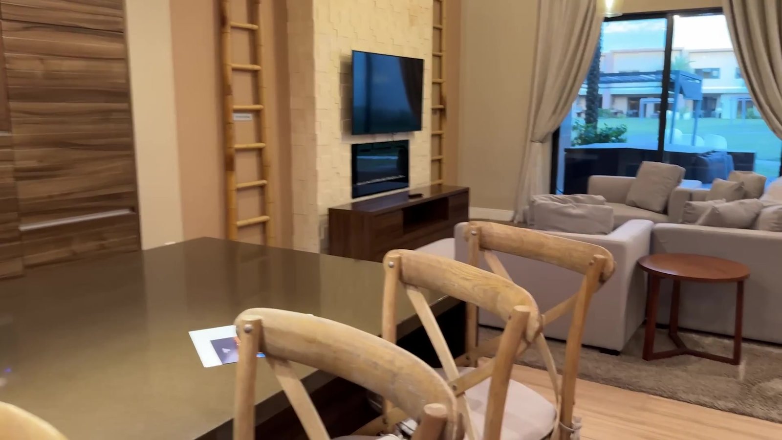 Sala de estar da casa do Magic Village com sofá claro, TV e mesa de jantar de madeira
