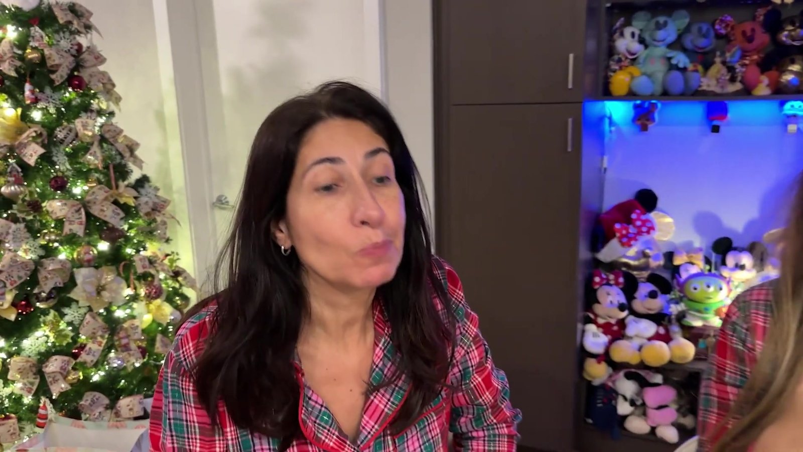 Mãe da Gabi provando um dos chocolates da Universal na mesa da prova, com árvore de Natal ao fundo