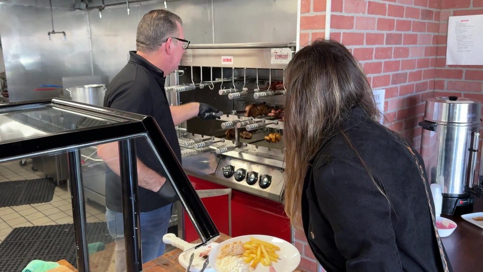 Churrasqueiro do Laçador Grill cortando a carne na chapa enquanto Gabi espera com o prato