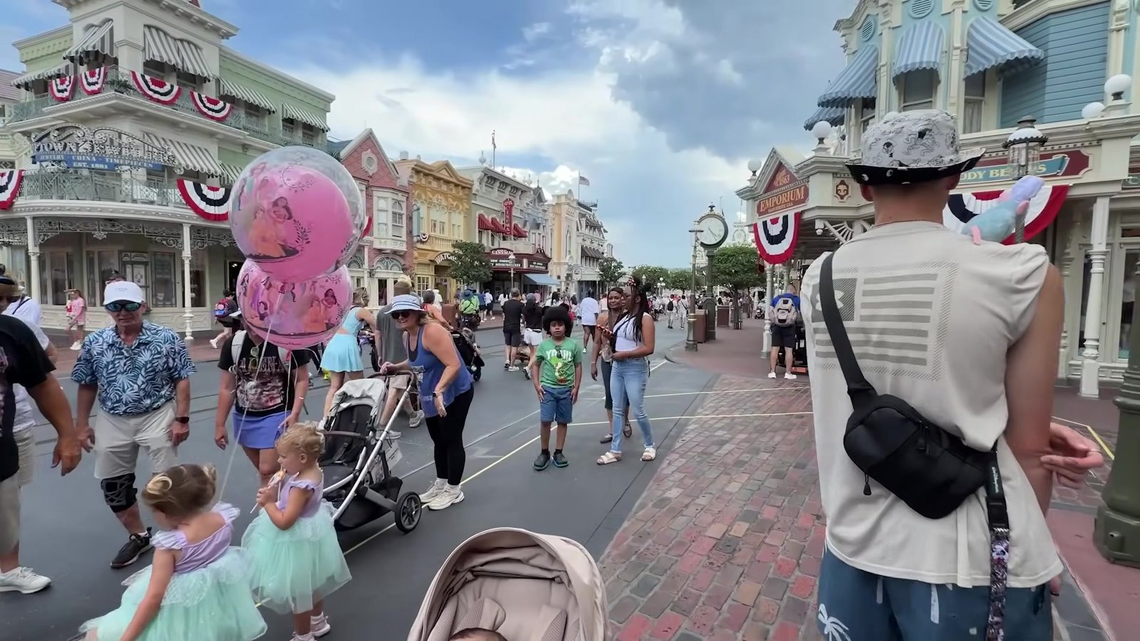 Main Street do Magic Kingdom cheia de visitantes em dia de sol, com balões e carrinhos de bebê