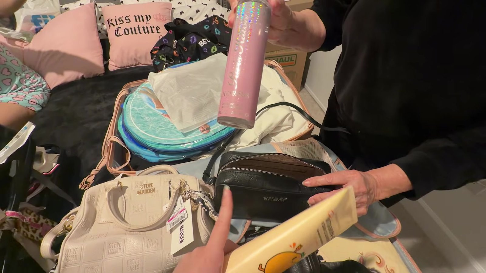 Garrafa Stanley rosa sendo colocada na mala junto com bolsas e cosméticos