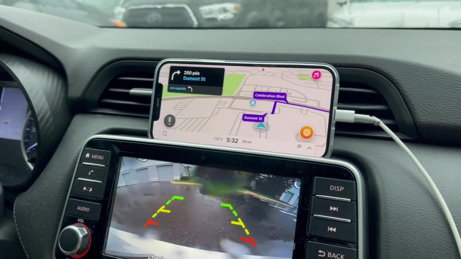 Celular com o Waze no painel do carro e câmera de ré na tela, saindo de Celebration