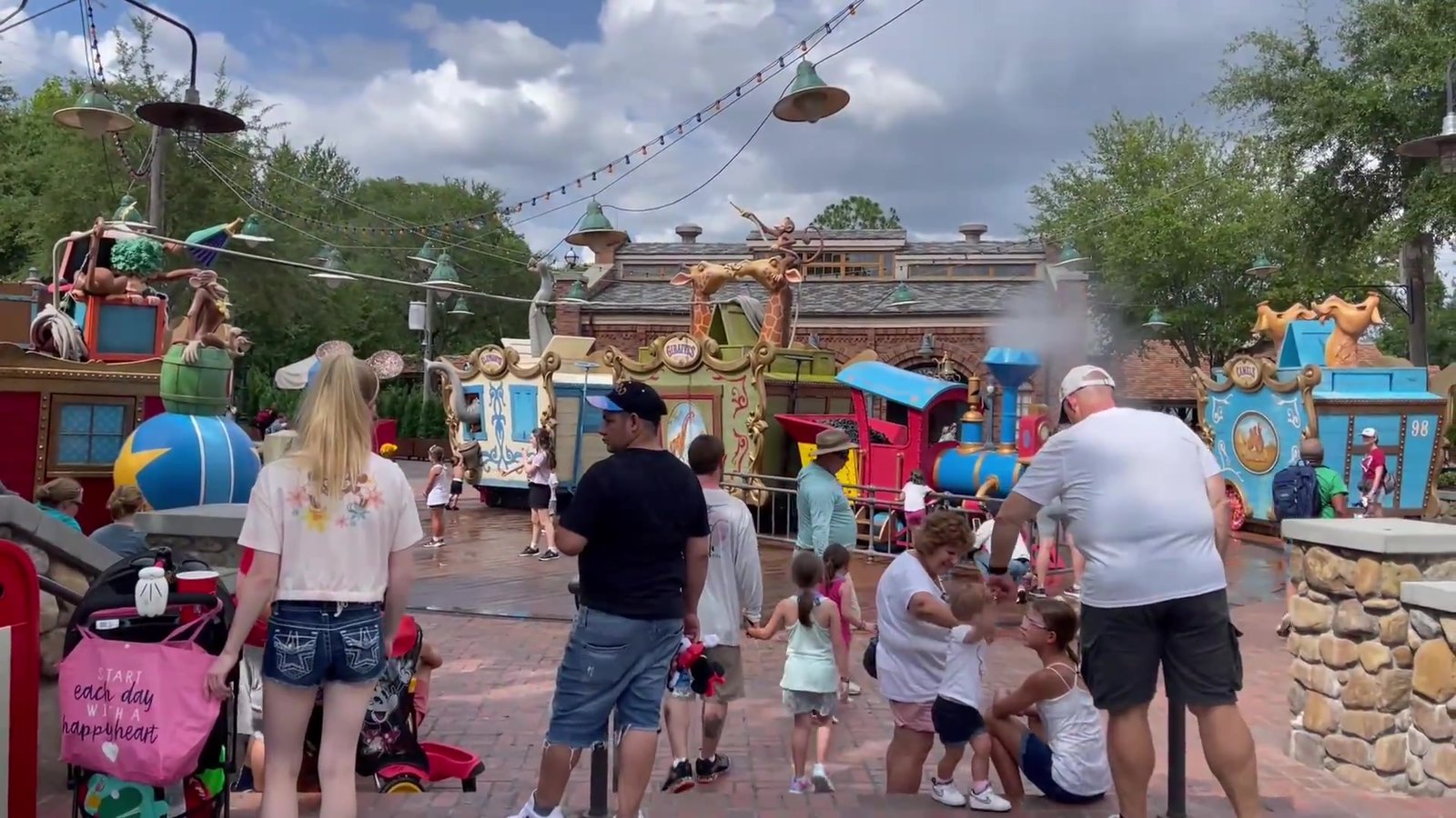 Crianças brincando na água da Casey Jr. Splash 'N' Soak Station, com o trem do circo ao fundo