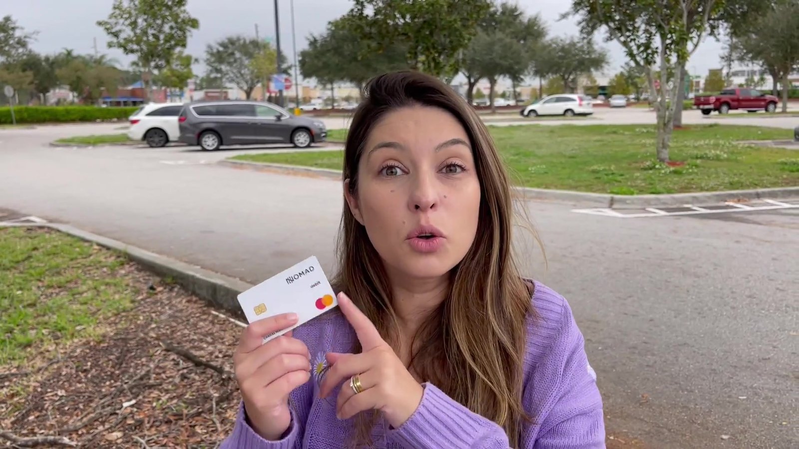 Gabi mostrando o cartão físico da conta em dólar no estacionamento do Walmart