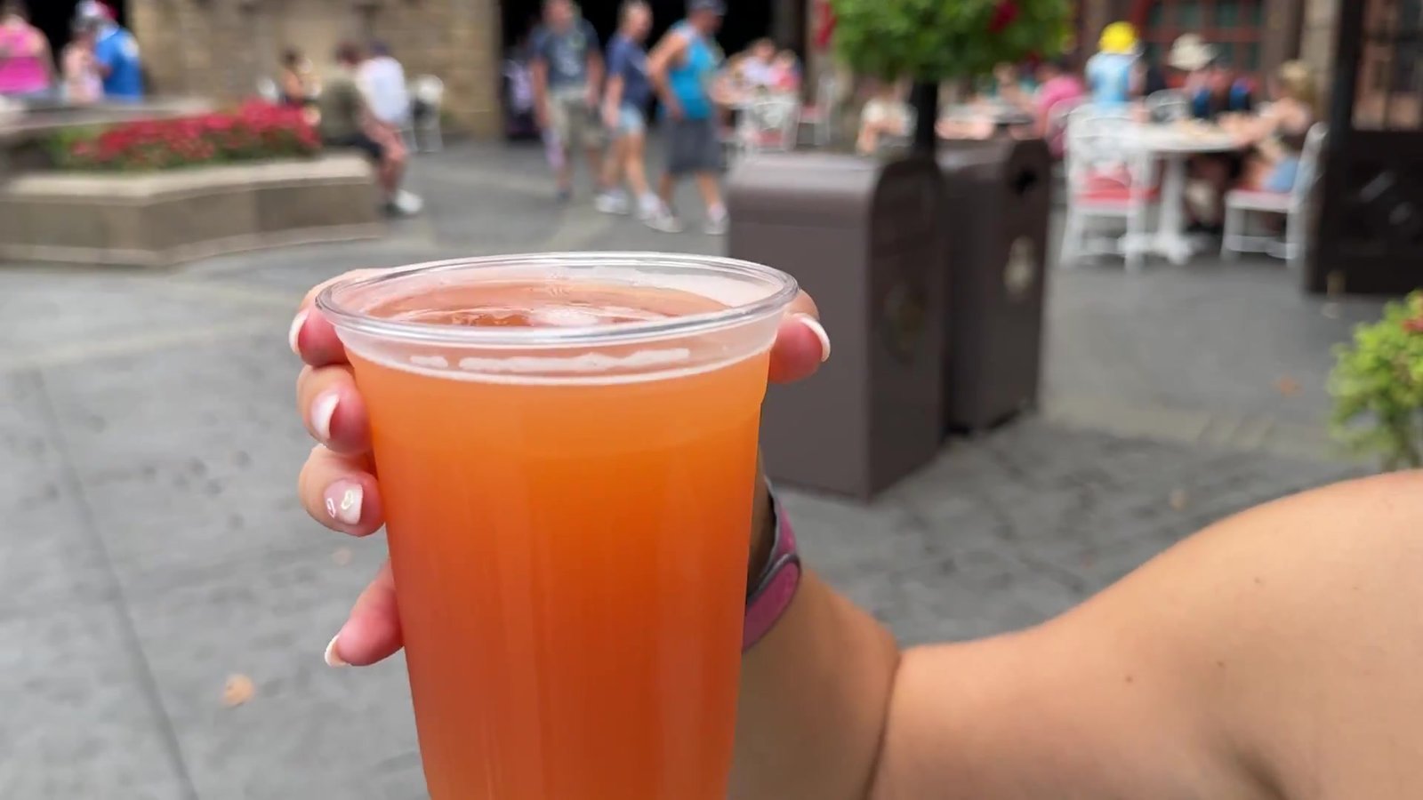 Copo com drink de frutas cor de laranja na mão da Gabi, andando pelo World Showcase do Epcot