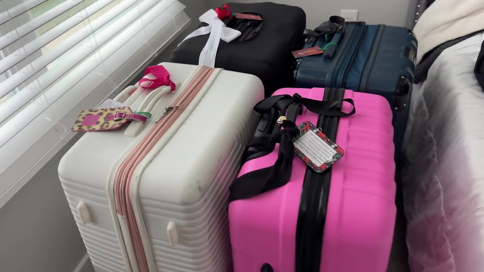 Malas grandes rosa, branca e azul prontas e etiquetadas no quarto antes de ir pro aeroporto