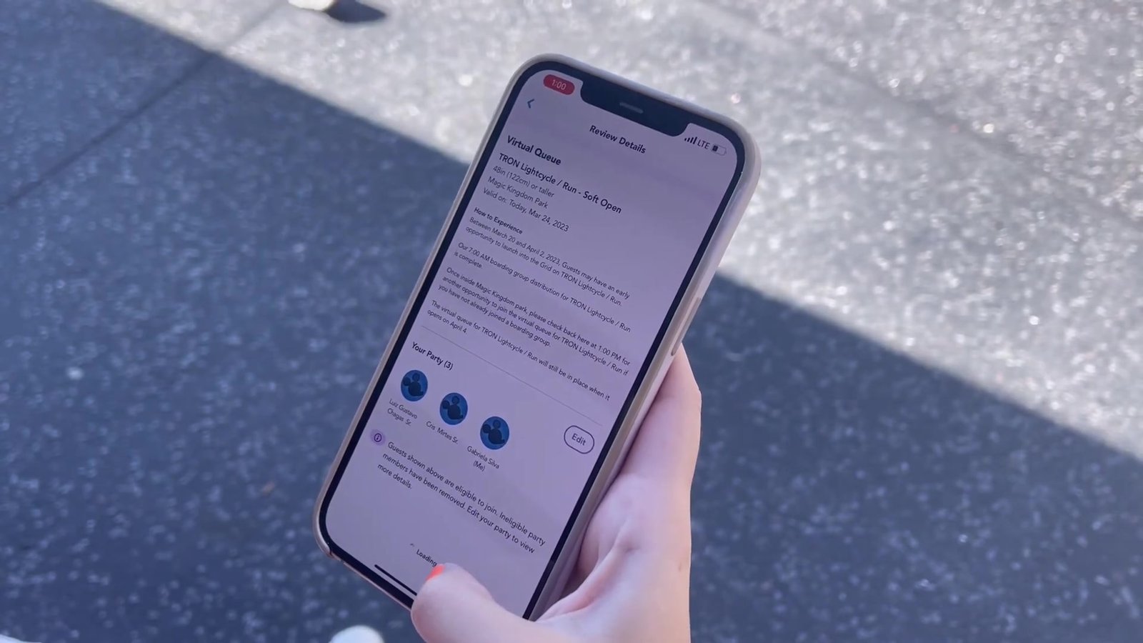 Mão segurando o celular ao sol com a confirmação da fila virtual do TRON Lightcycle / Run no app
