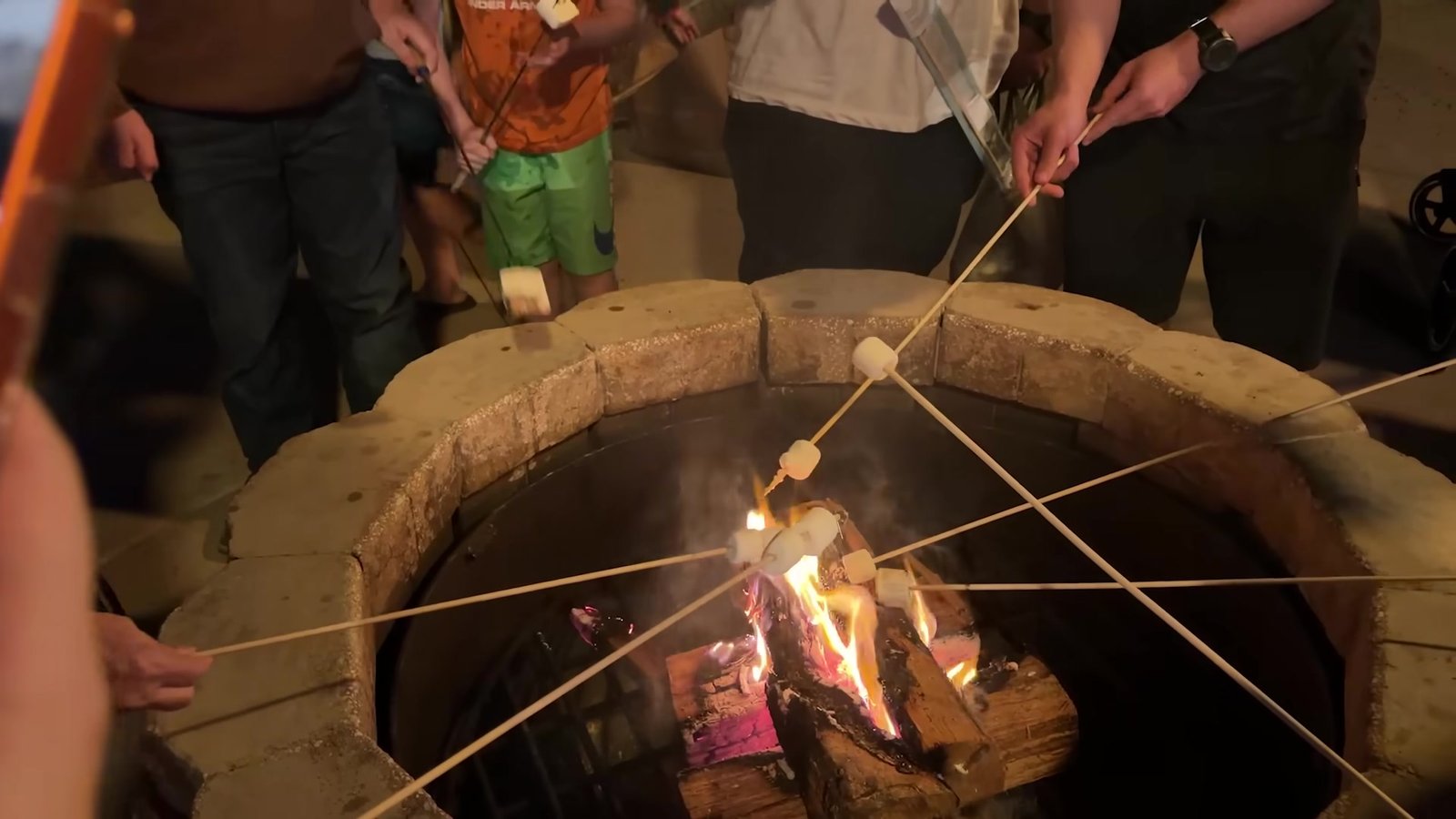 Várias pessoas tostando marshmallows nos palitos sobre a fogueira de pedra do Fort Wilderness