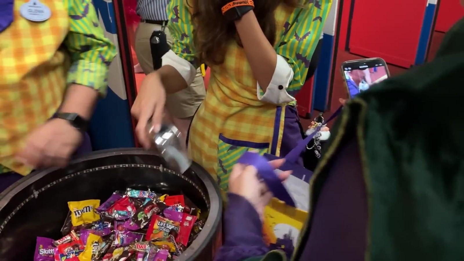 Cast Members entregando punhados de M&M's, Snickers e Skittles de um balde na festa de Halloween da Disney