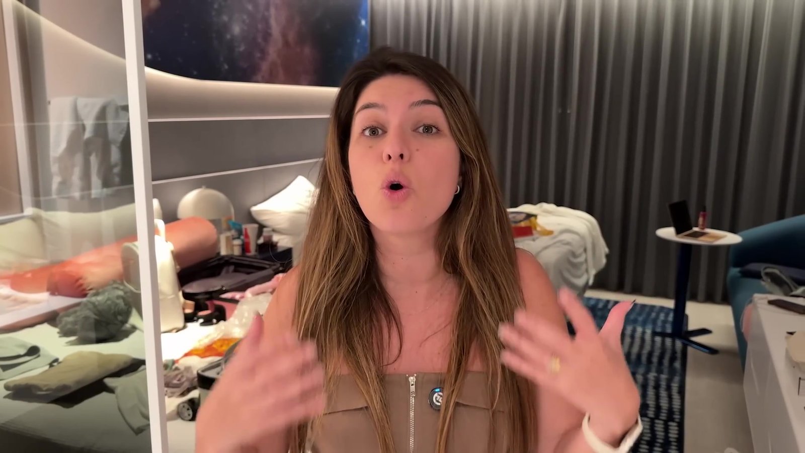 Gabi mostrando o quarto do Helios, com a cama e a cortina do janelão