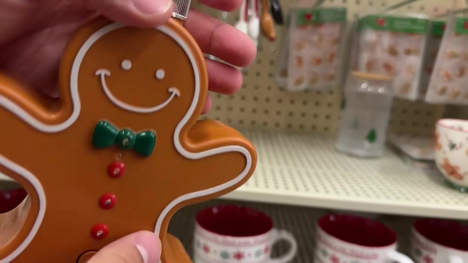 Boneco de gengibre decorativo com gravata verde na mão, com canecas de Natal ao fundo