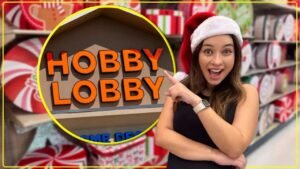 Gabi do Turistorlando de gorro de Papai Noel apontando para o letreiro da Hobby Lobby