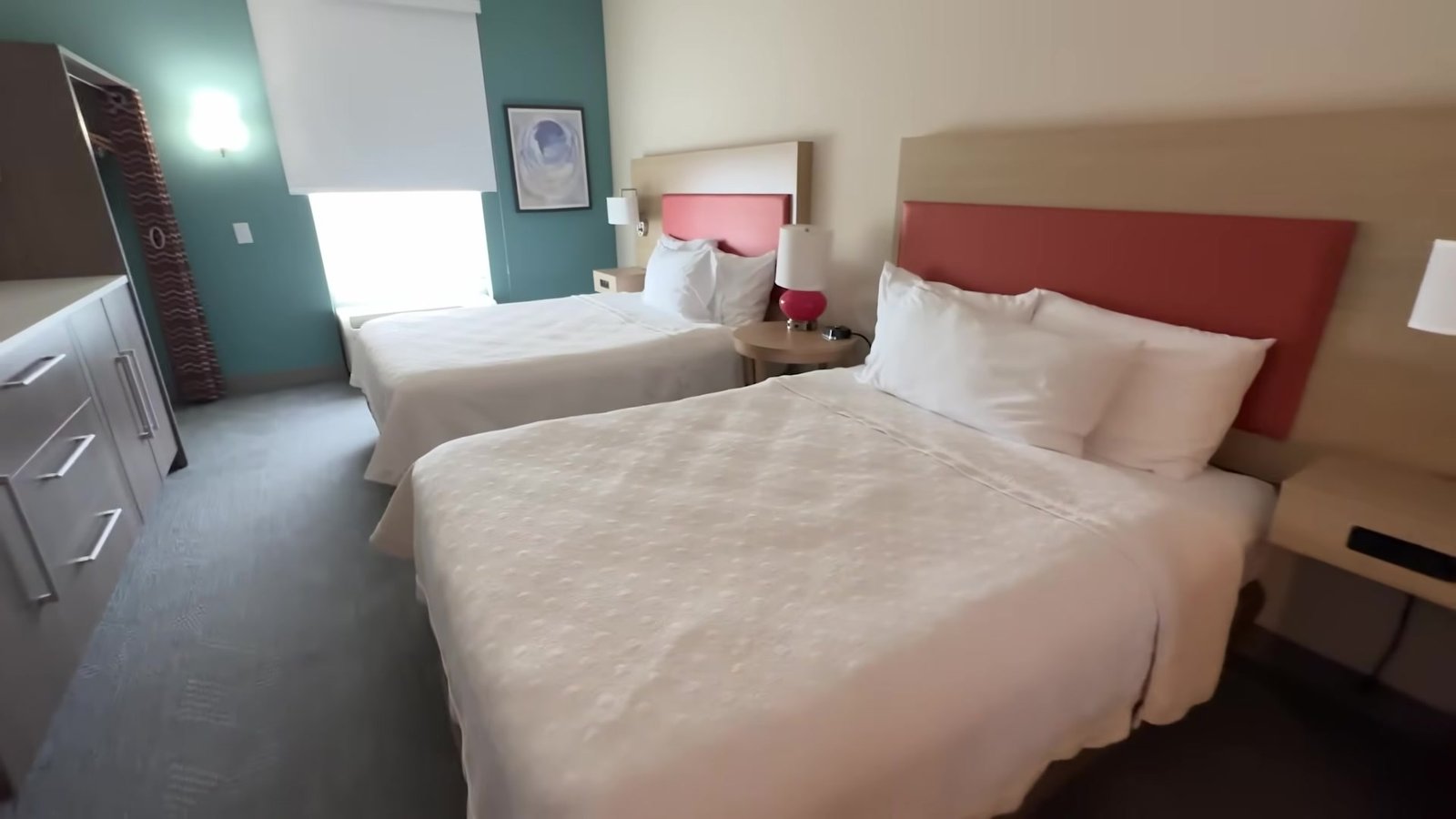 Quarto do Home2 Suites com duas camas de casal, cabeceiras vermelhas e parede verde