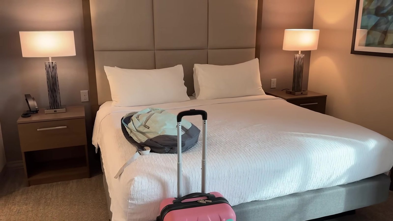 Cama king do quarto do Homewood Suites, com mala na cama e cabeceira estofada