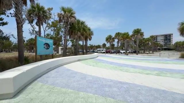 Calçada larga e pavimentada na entrada da Siesta Beach, com o estacionamento gratuito ao fundo