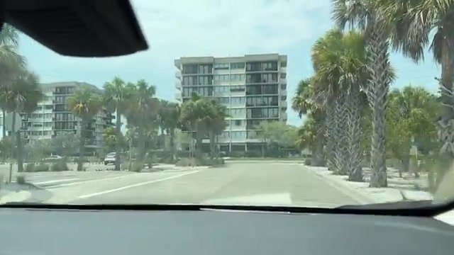 Prédios baixos de apartamentos e palmeiras na avenida principal de Siesta Key, vistos de dentro do carro