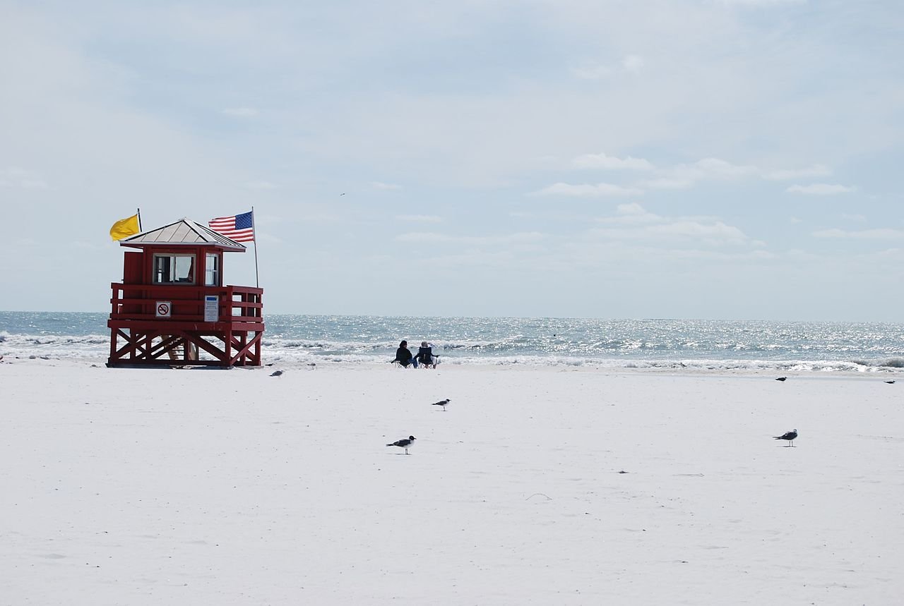 Areia branca de quartzo da Siesta Beach com posto de salva-vidas vermelho e gaivotas