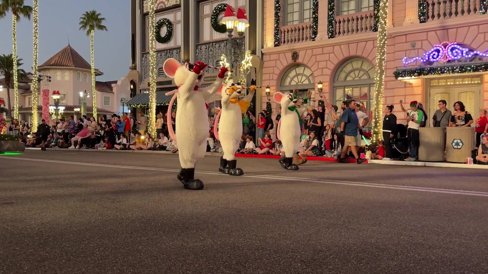 Dançarinos fantasiados de ratinhos brancos com bengalas doces desfilando na rua iluminada do Universal Studios durante a parada de Natal