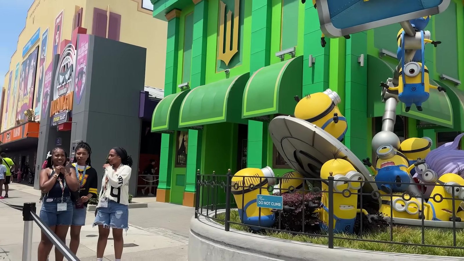 Fachada verde da Minion Land com Minions gigantes pendurados na decoração e visitantes tirando foto