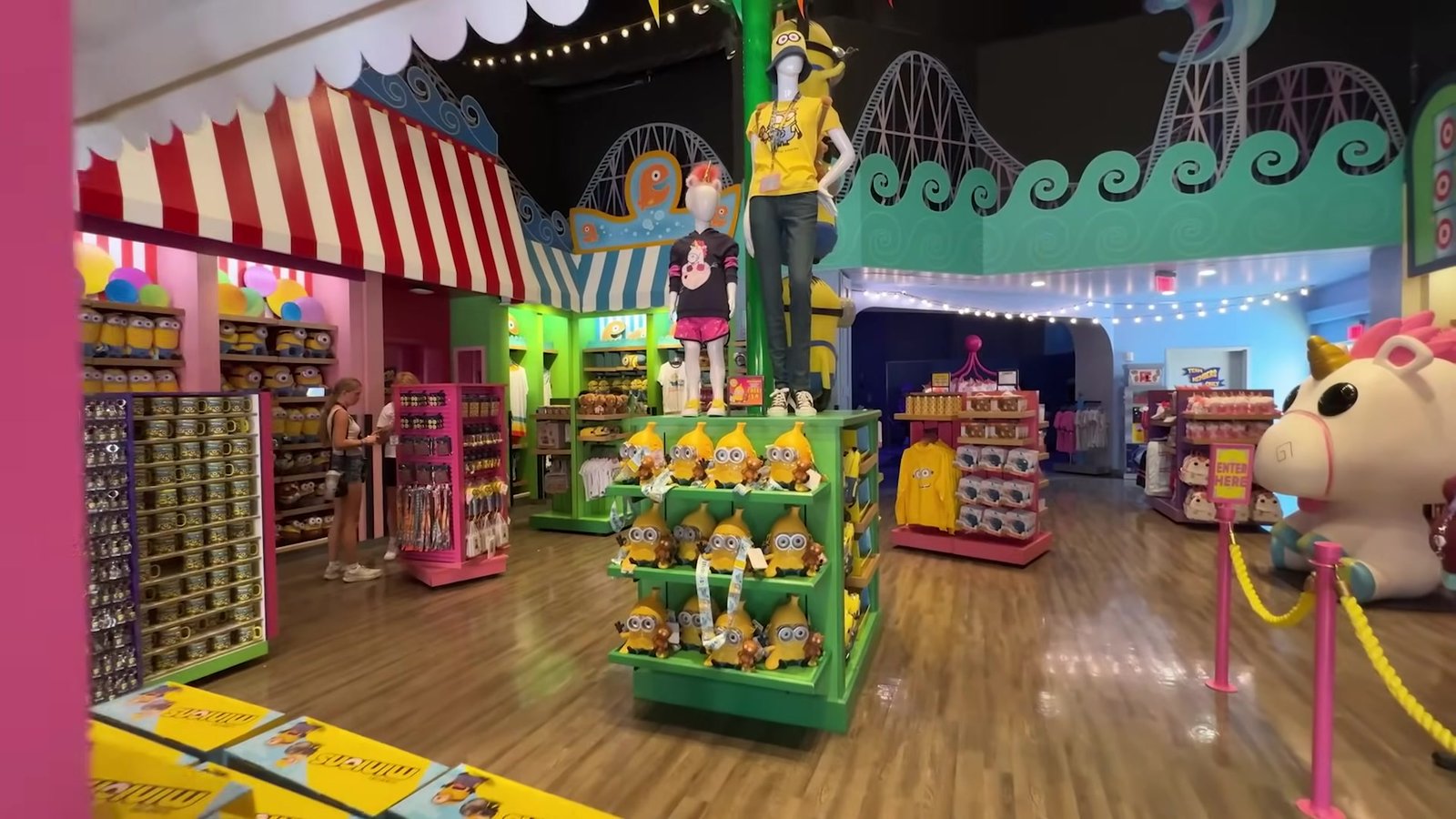 Interior da loja da Minion Land com pilhas de pelúcias de Minions, unicórnio gigante e listras coloridas