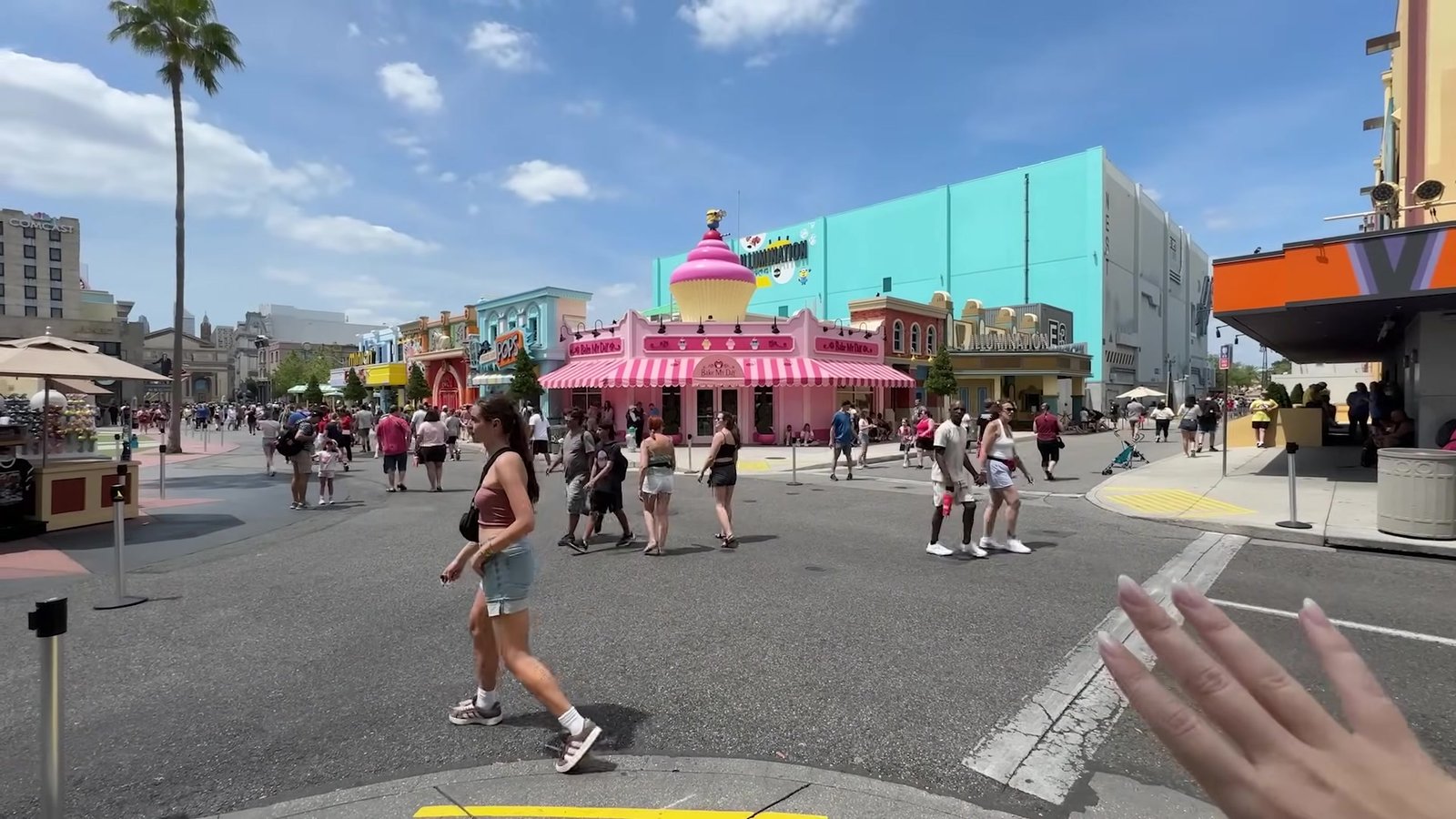 Rua da Minion Land com a fachada rosa listrada da confeitaria Bake My Day e visitantes passando
