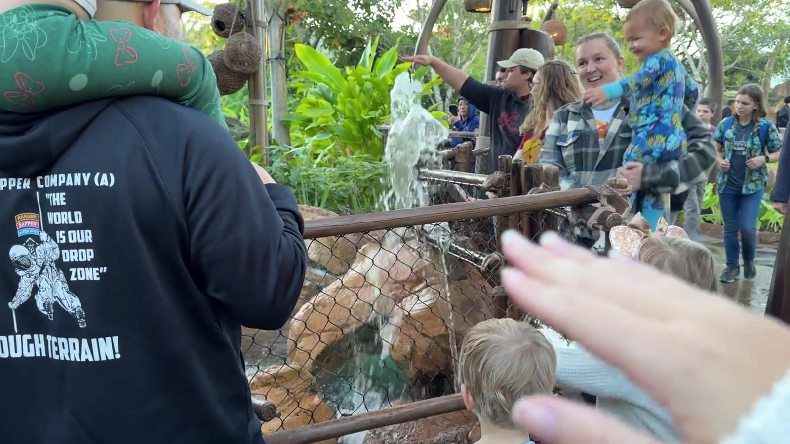 Crianças e adultos erguendo as mãos para brincar com o jato de água na Journey of Water do Epcot