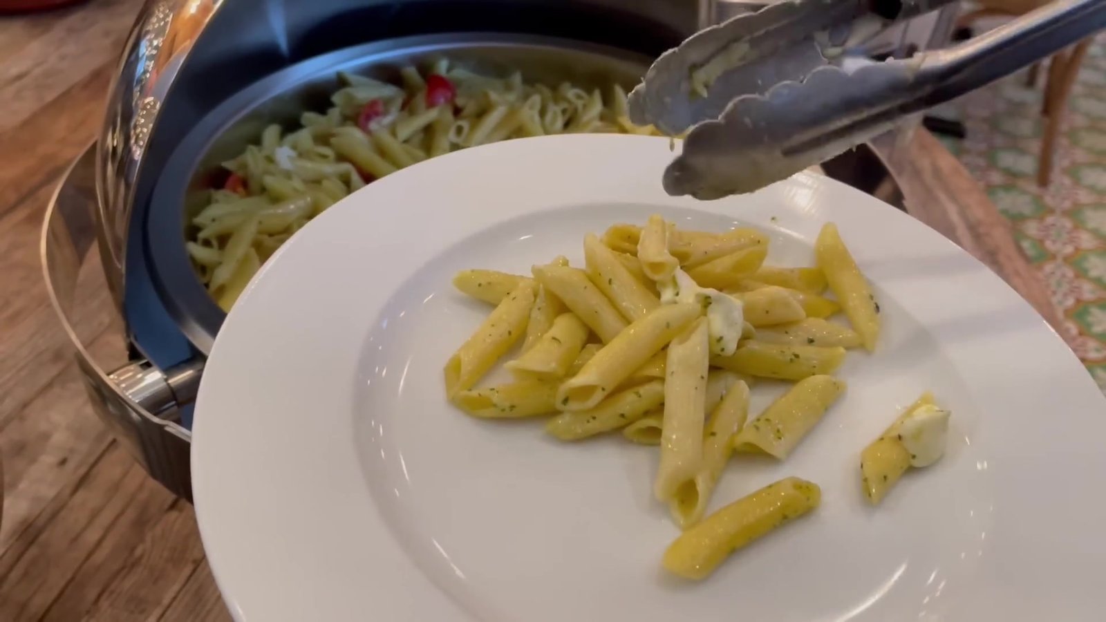Penne com molho de ervas sendo servido no prato com a pinça do buffet