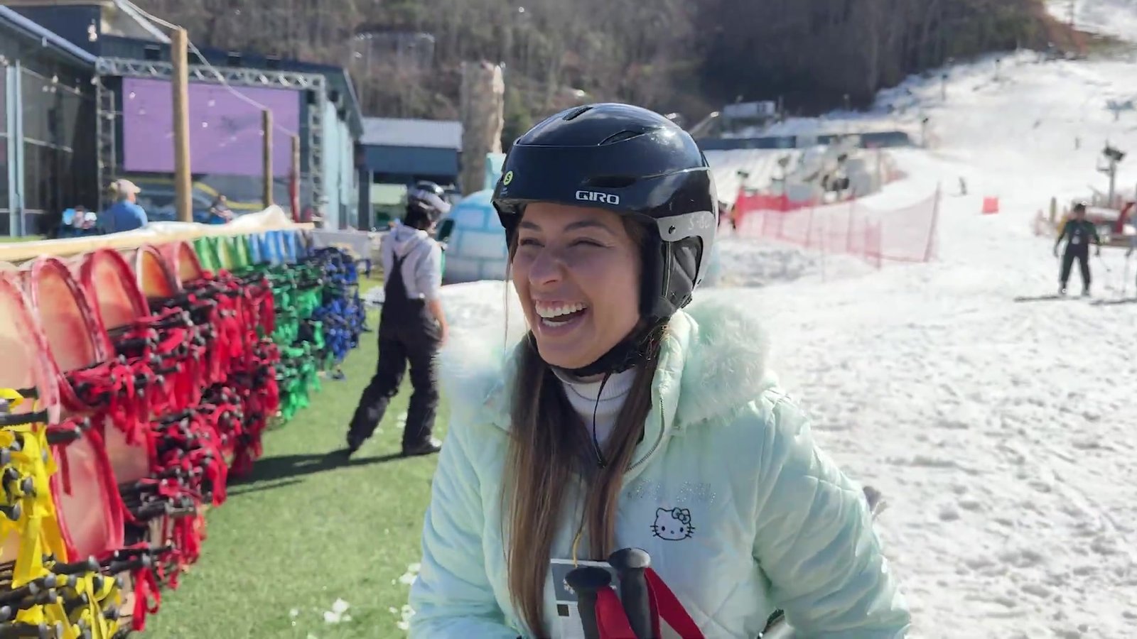 Gabi de capacete ao lado dos trenós coloridos e da pista de neve da Ober Mountain