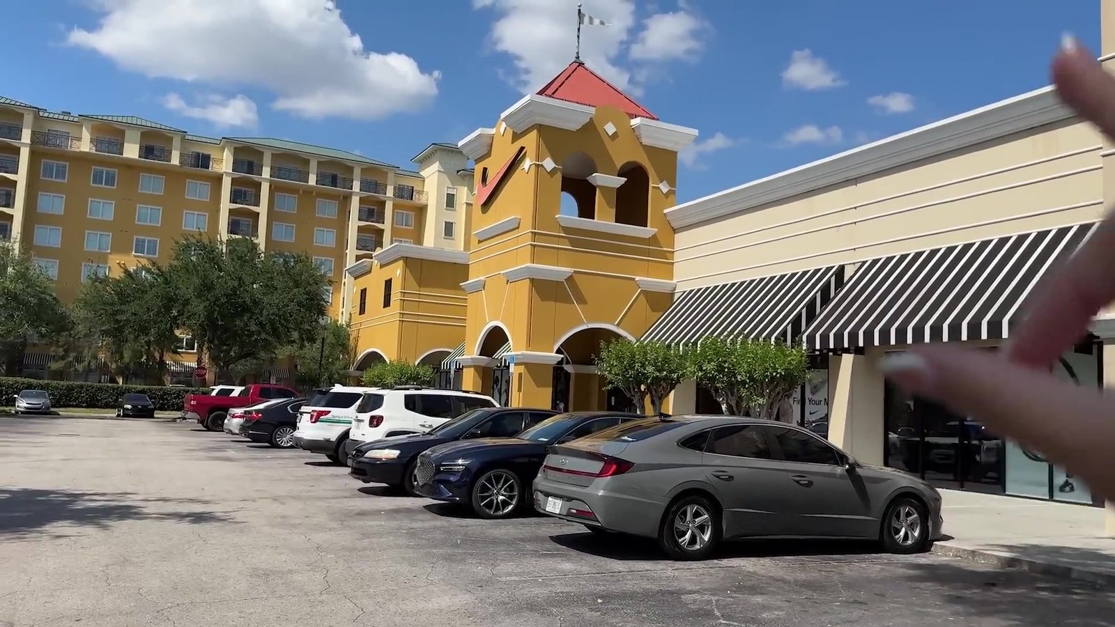 Fachada do Lake Buena Vista Factory Stores com a torre amarela da Nike e carros estacionados na frente das lojas