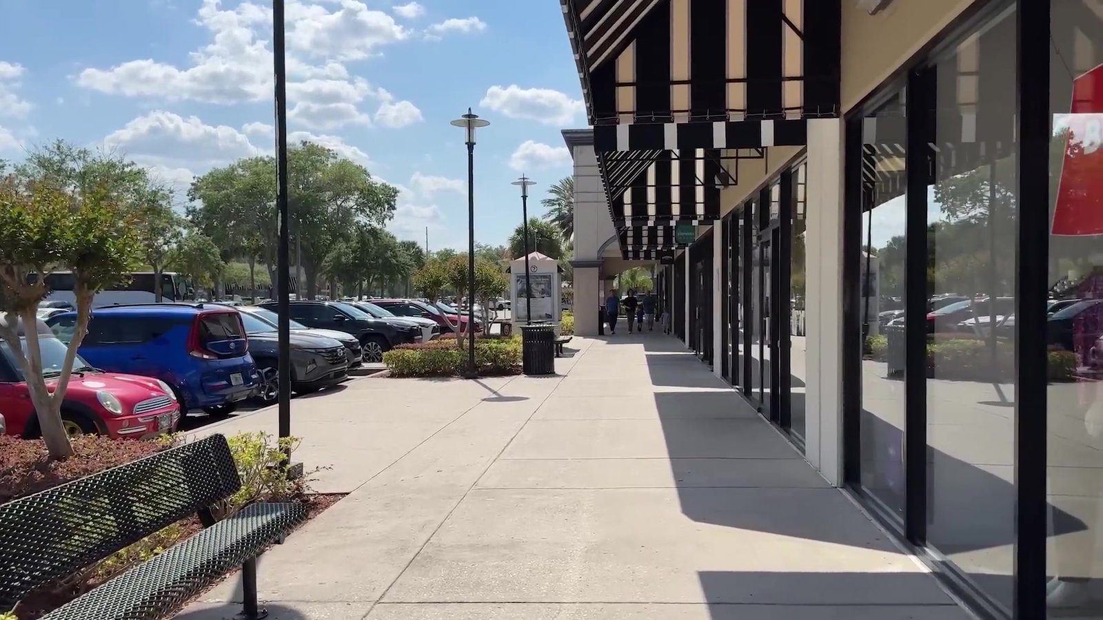 Calçada do outlet Lake Buena Vista com bancos, jardim e carros estacionados ao lado