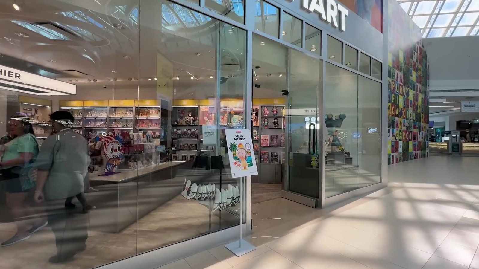 Fachada de vidro da primeira loja Pop Mart de Orlando, dentro do shopping, com as prateleiras de colecionáveis ao fundo