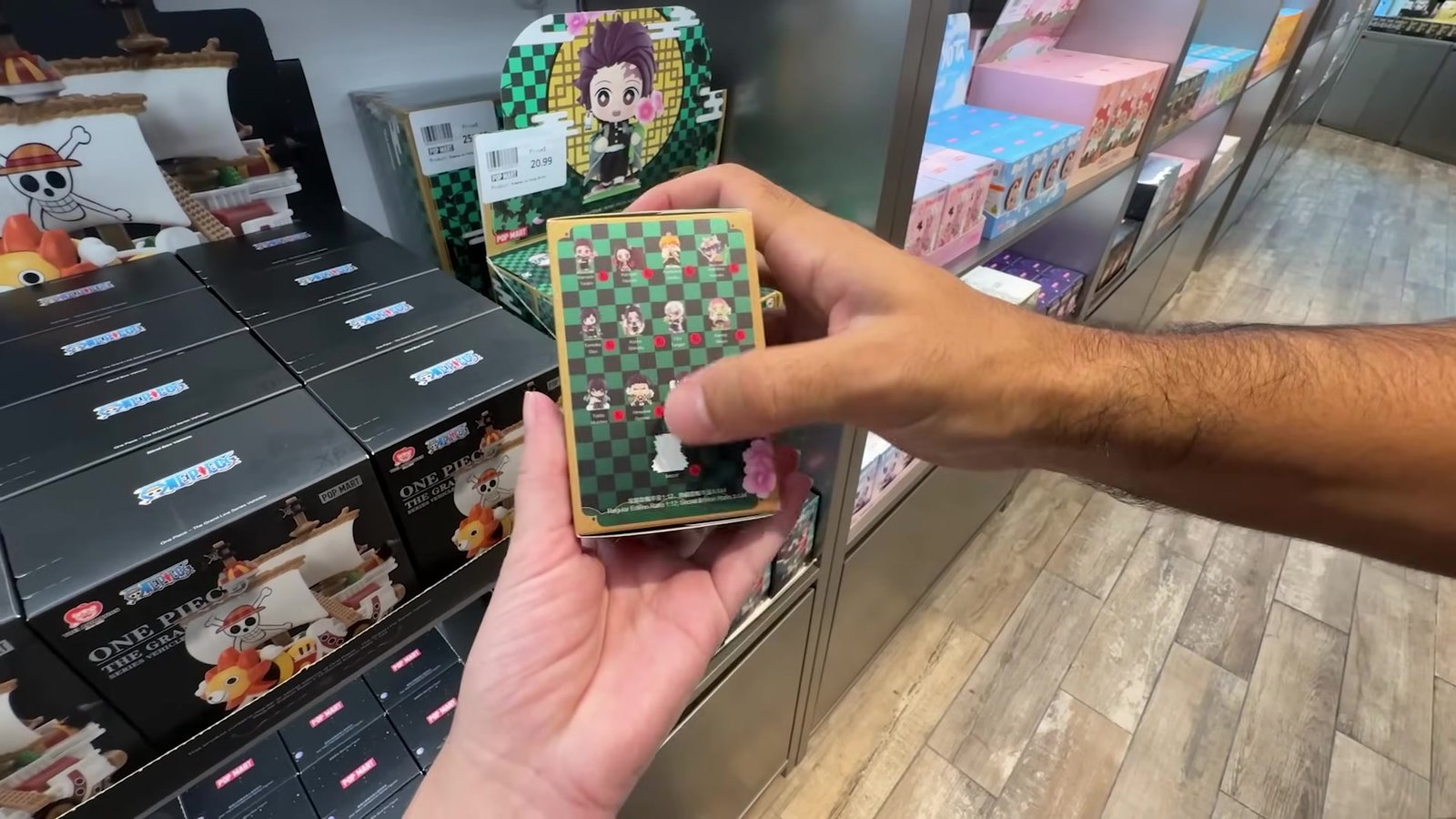 Mão segurando uma caixa-surpresa da série Demon Slayer na frente das caixas de One Piece na Pop Mart