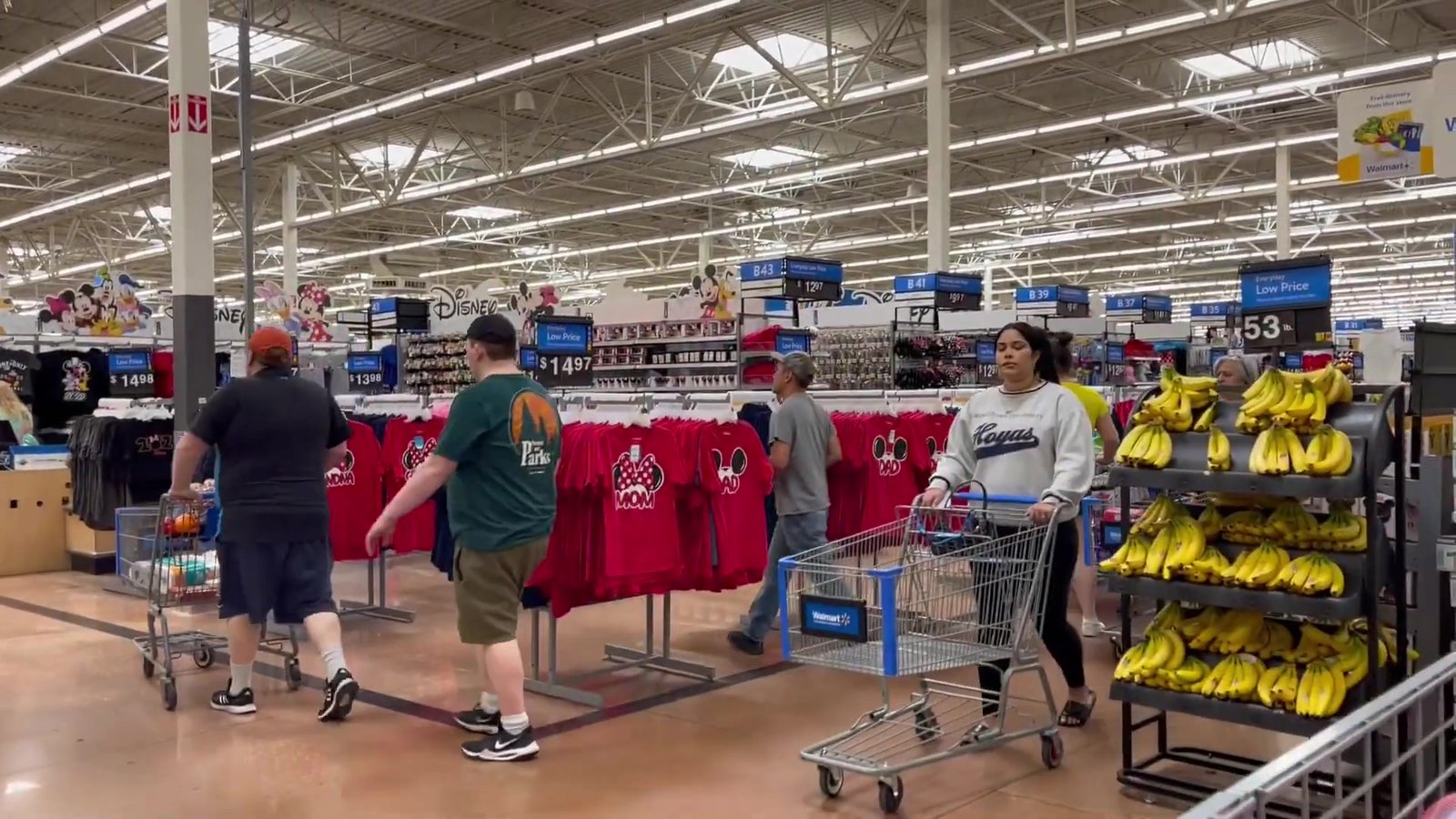 Visão geral do corredor da Universal no Walmart de Orlando, com araras de camisetas da Grifinória e dos Minions