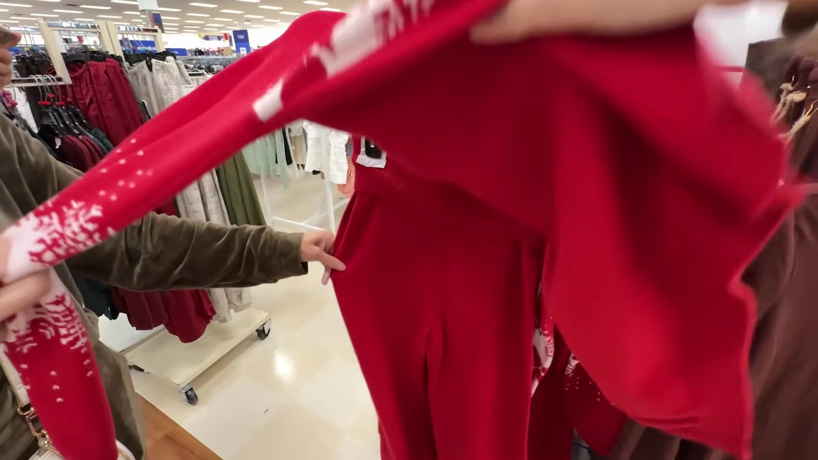 Gustavo abrindo um blusão plush vermelho com flocos de neve na arara da Marshalls