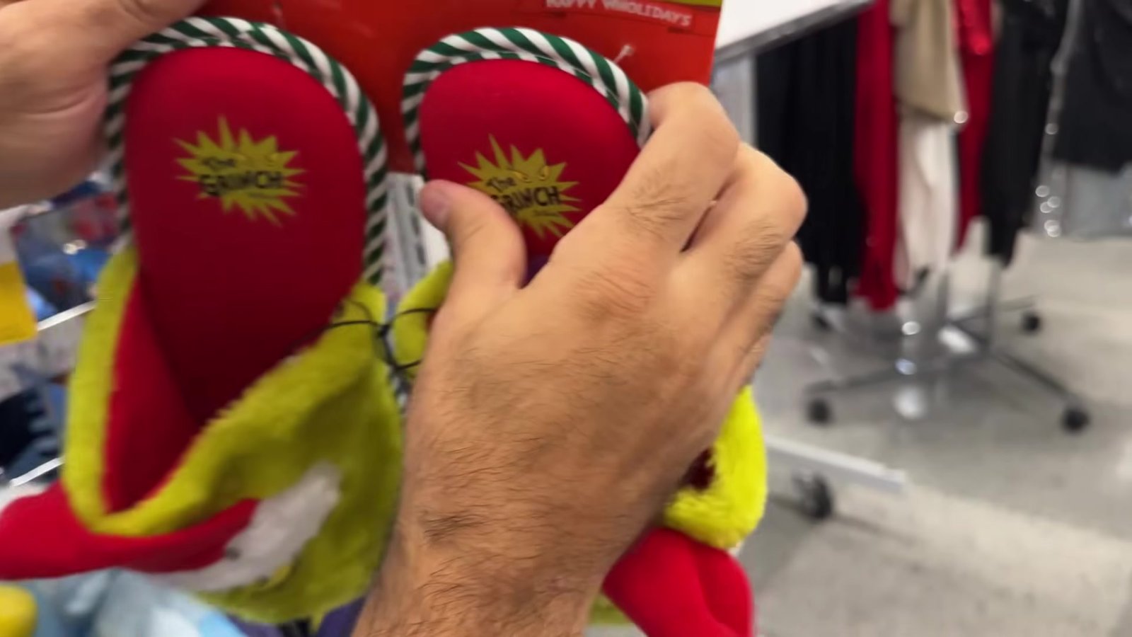 Par de pantufas do Grinch com sola vermelha na mão, na loja Ross em Orlando