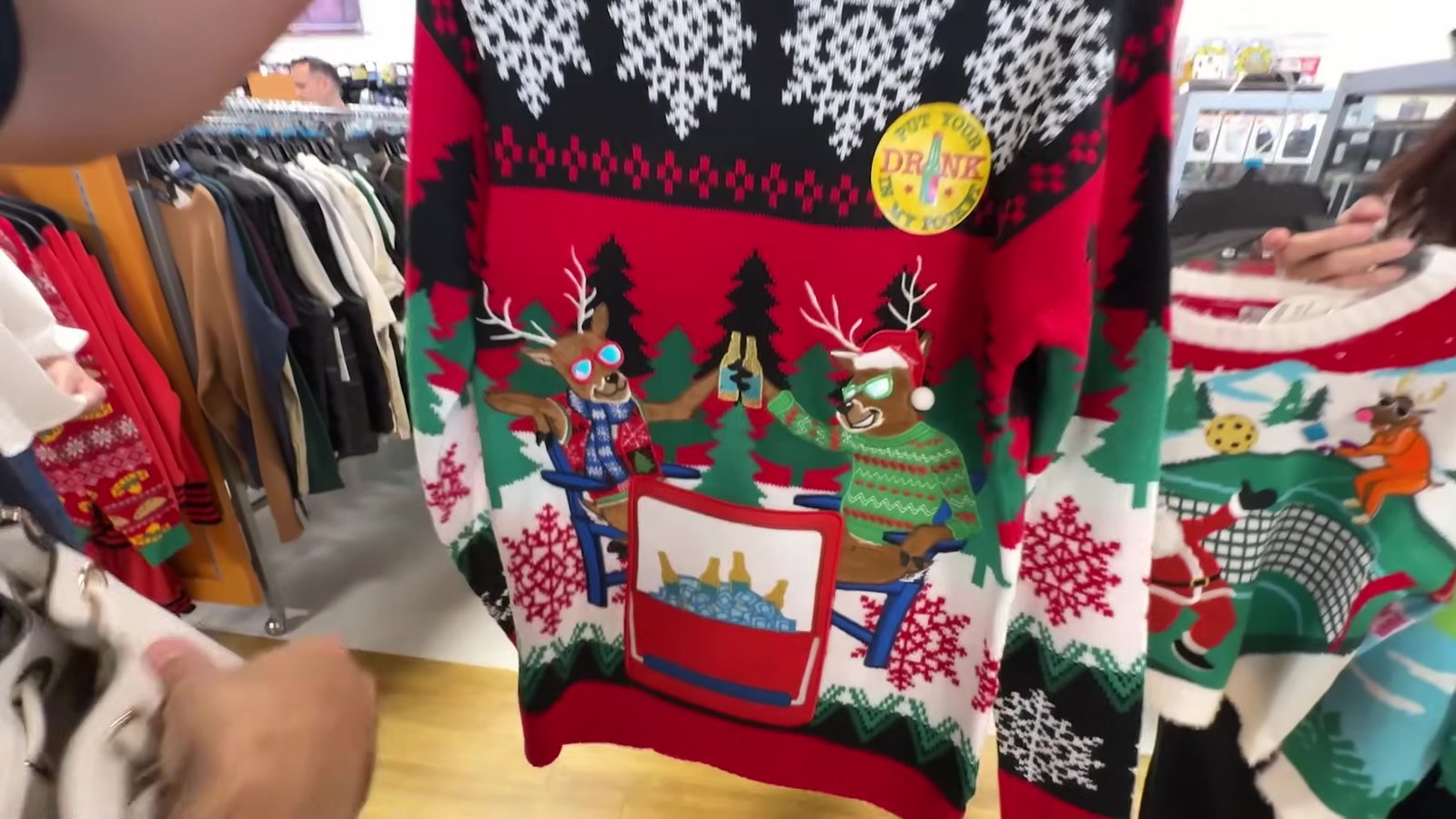 Ugly sweater vermelho com renas e flocos de neve sendo mostrado na TJ Maxx de Orlando
