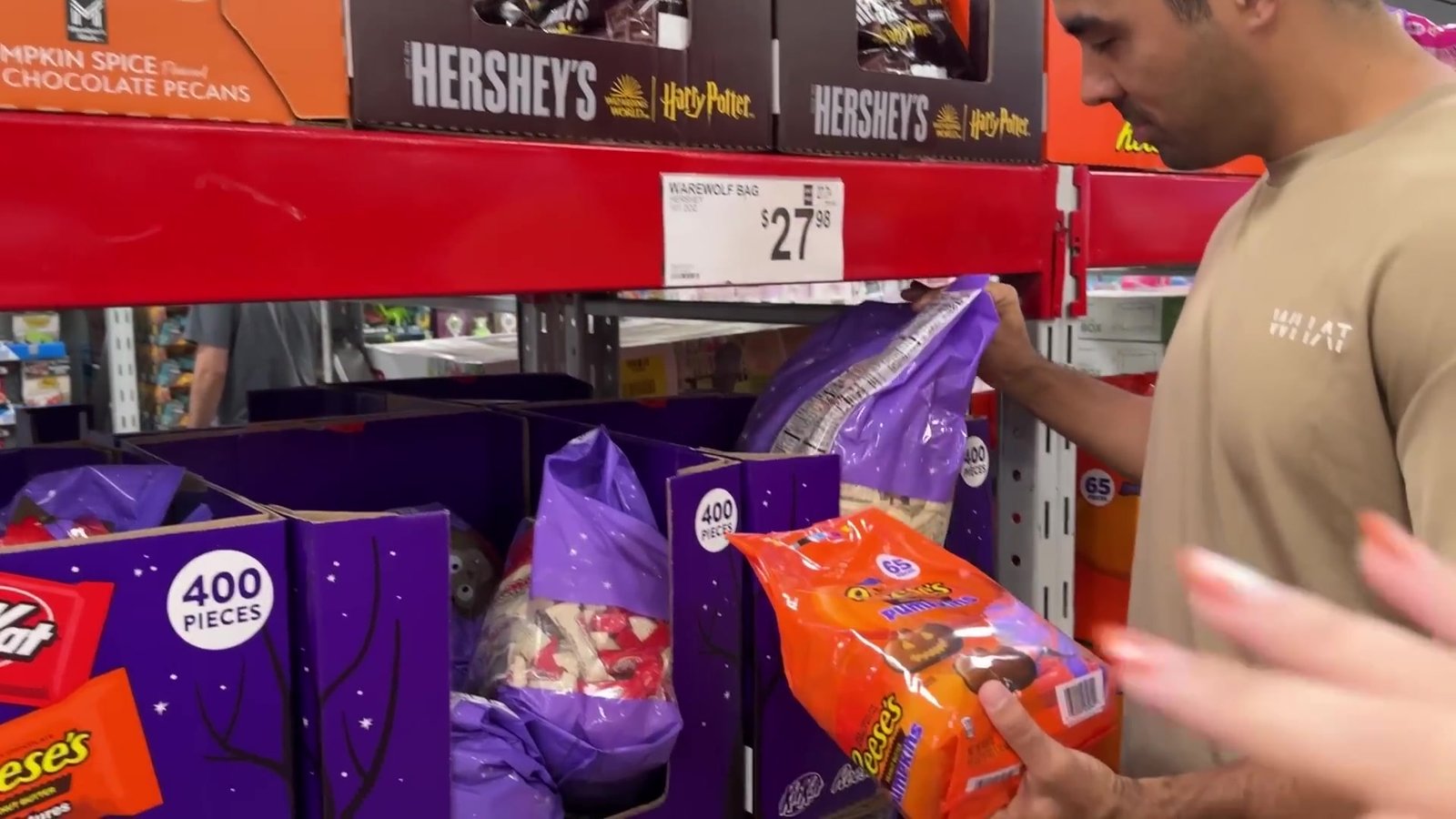 Gustavo pegando um pacote de Reese's na prateleira de doces de Halloween do Sam's Club, com sacos de 400 unidades
