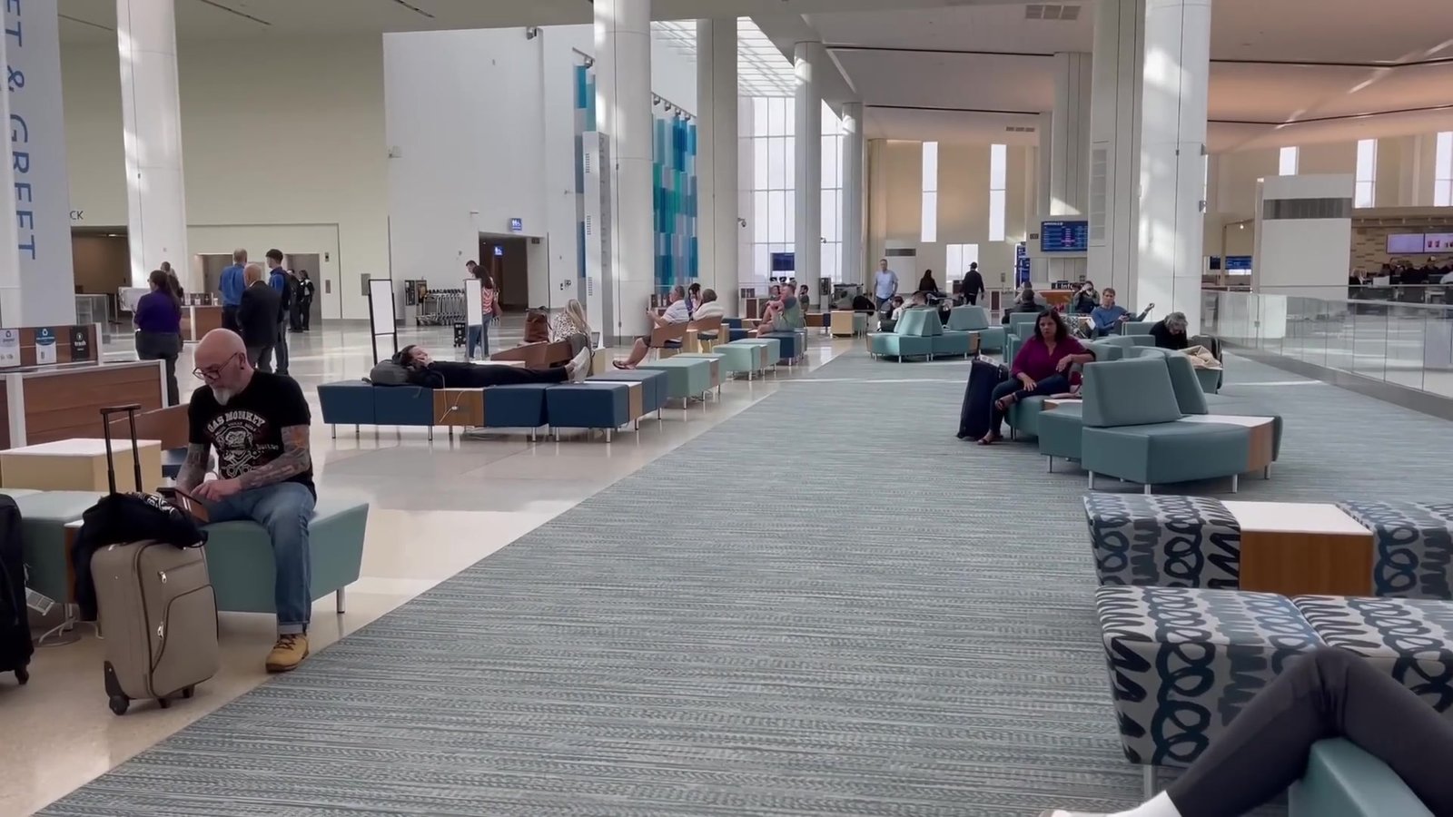 Área de espera do Terminal C com sofás e passageiros sentados com malas