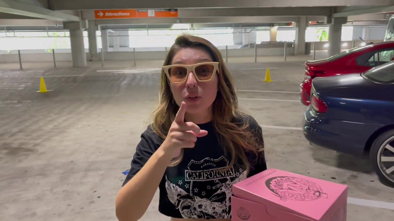 Gabi no estacionamento da Universal segurando a caixa rosa da Voodoo Doughnut