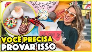 Gabi segurando a caixa rosa da Voodoo Doughnut com donuts coloridos e o Voodoo Doll em destaque