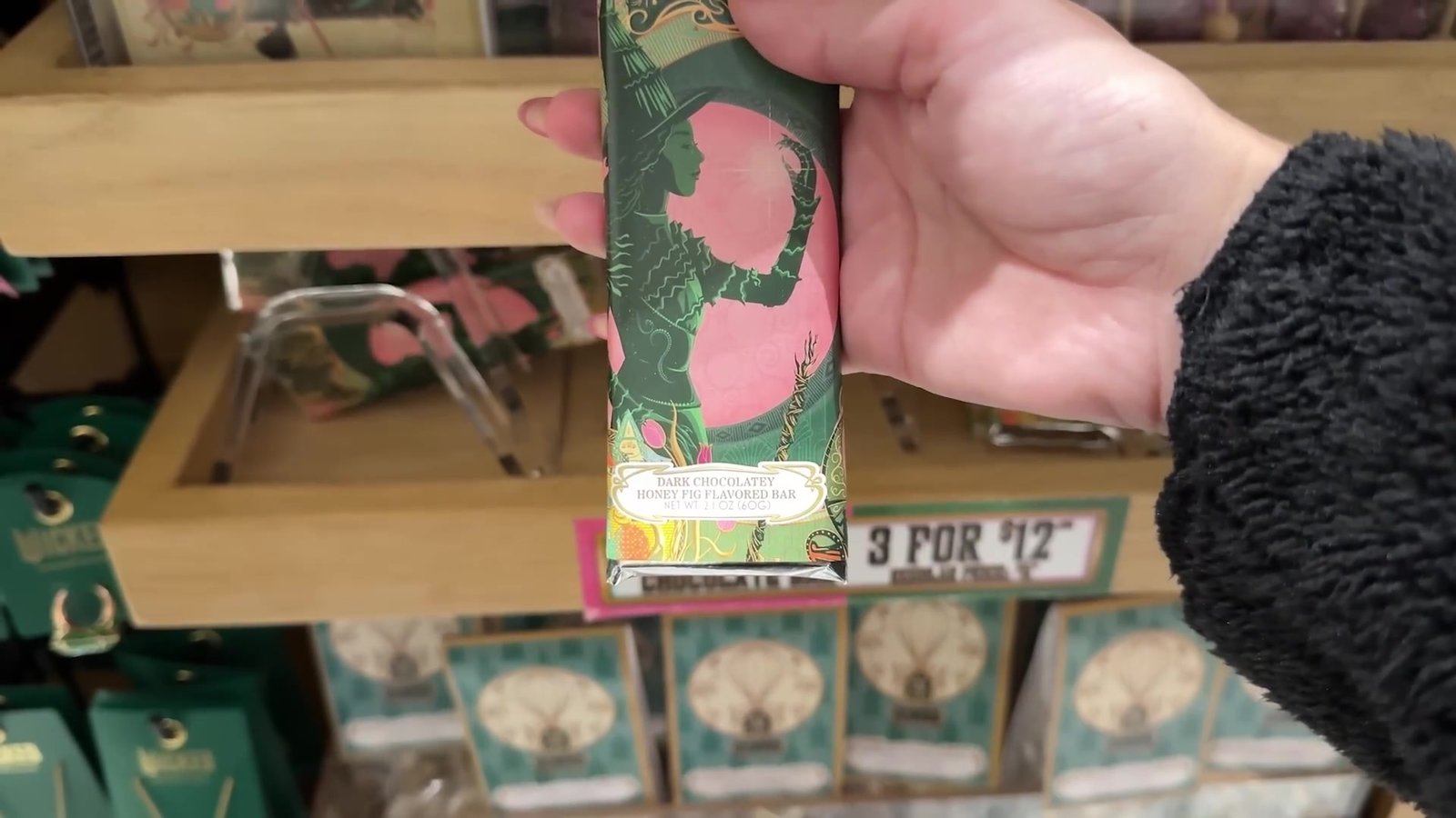 Barra de chocolate de Wicked na mão, com a placa de 3 por 12 dólares na prateleira